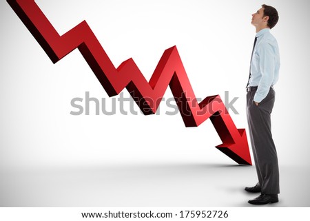 Serious businessman standing with hands in pockets against red arrow pointing down