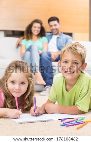 Happy siblings colouring on the rug with parents watching from sofa at home in living room