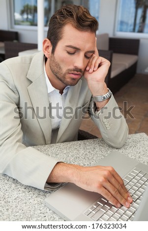 Exhausted businessman working with his laptop at table in patio of restaurant