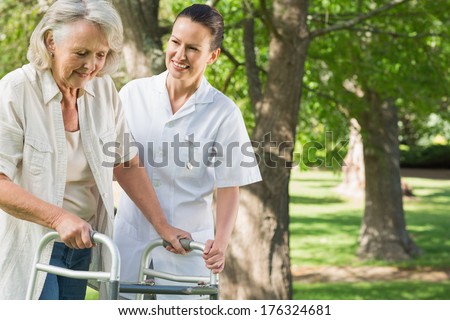 Smiling young female assisting mature woman with walker at the park
