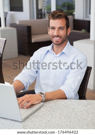 Smiling businessman working on laptop at table in outdoor patio of restaurant