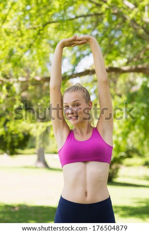 Portrait of a healthy and beautiful young woman in sports bra stretching hands up in the park