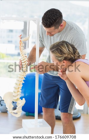 Male instructor pointing on a bone in the spine to woman at gym