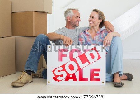 Happy couple sitting on floor with sold sign in their new home