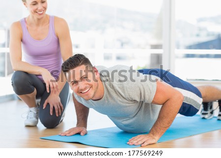 Portrait of handsome man doing push ups with female trainer in fitness studio