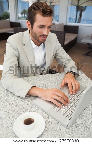 Happy businessman working with his laptop at table having coffee in patio of restaurant