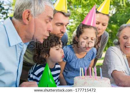 Cheerful extended family wearing party hats and blowing birthday cake in the park