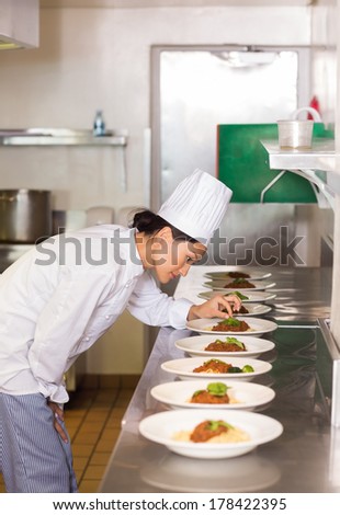 Side view of a concentrated female chef garnishing food in the kitchen
