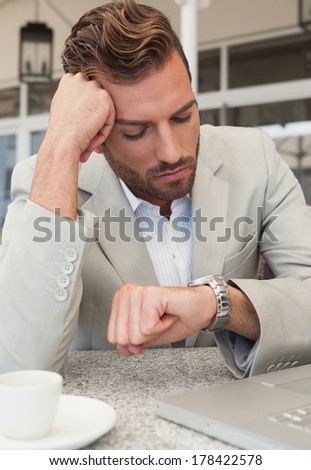 Frowning businessman looking at his watch in patio of restaurant