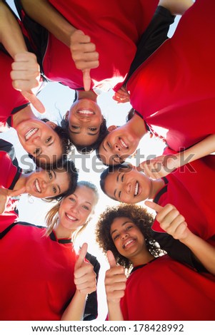 Directly below shot of female soccer team gesturing thumbs up while forming huddle against clear sky