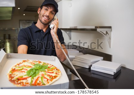 Smiling pizza delivery man taking an order over the phone showing a pizza in a commercial kitchen
