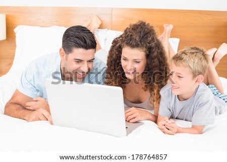 Happy family using laptop together on bed at home in bedroom