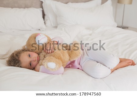 Portrait of a young girl with stuffed toy resting in bed at home