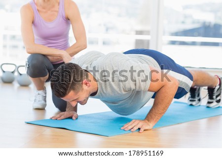 Female trainer helping man with push ups at gym