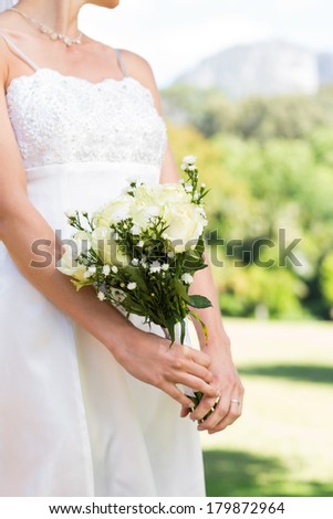 Midsection of bride holding flower bouquet while standing in garden