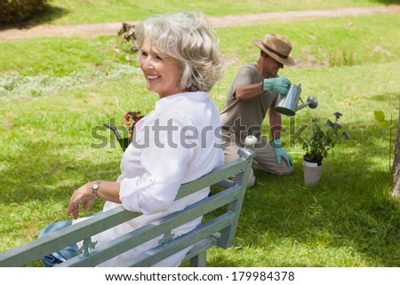 Happy woman sitting on bench while man watering young plant at the park