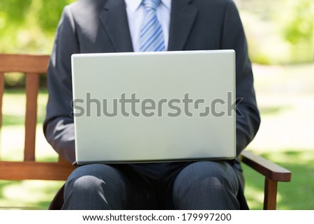 Midsection of businessman using laptop while sitting on park bench
