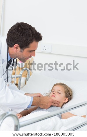 Young male doctor examining thyroid glands of sick girl in hospital ward