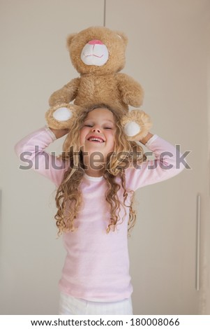 Portrait of a young happy girl holding stuffed toy over head at home