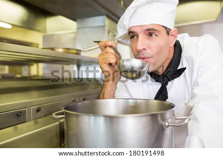 Concentrated young male cook tasting food in the kitchen