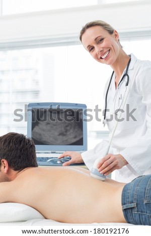 Happy female doctor performing ultrasound scan on back of male patient