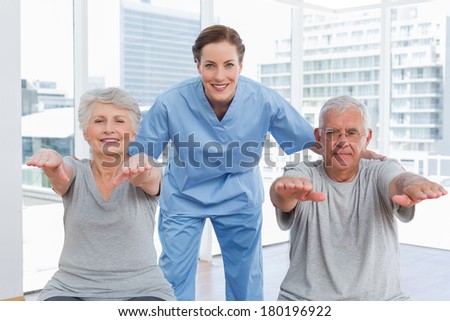 Portrait of a female therapist assisting senior couple with exercises in the medical office