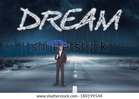 The word dream and businessman smiling at camera and holding blue umbrella against road leading out to the horizon