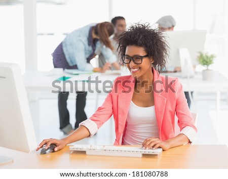Casual female artist using computer with colleagues in the background at a bright office
