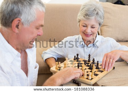 Senior couple sitting on floor playing chess at home in living room