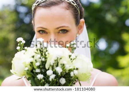 Closeup portrait of young bride peeking over flower bouquet in garden