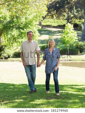 Full length of happy couple walking while holding hands in park