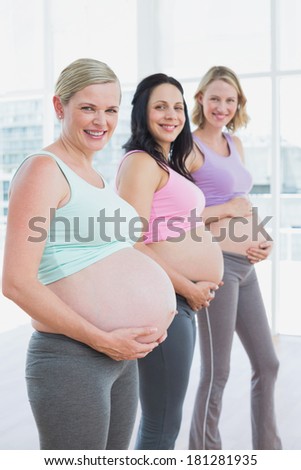 Happy pregnant women standing in a line holding their bumps in a fitness studio