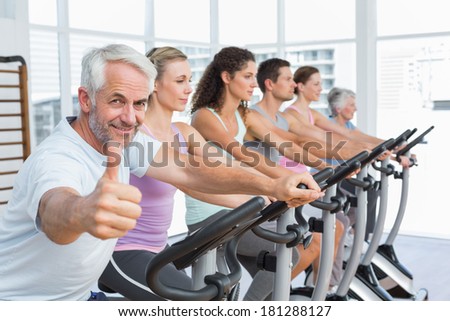 Man gesturing thumbs up with class working out at exercise bike class in gym