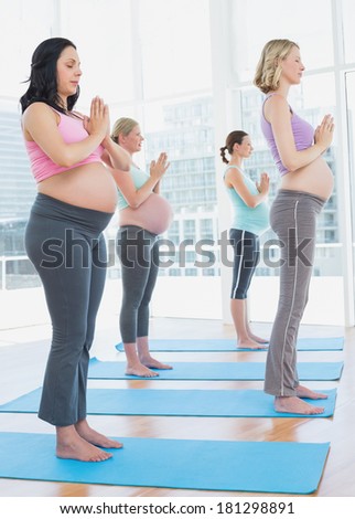 Pregnant women in yoga class standing in tree pose eyes closed in a fitness studio