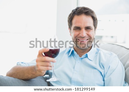 Happy man relaxing on sofa with glass of red wine at home in the living room