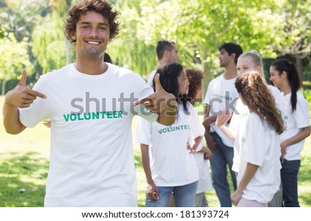 Portrait of male volunteer pointing at tshirt with friends in background