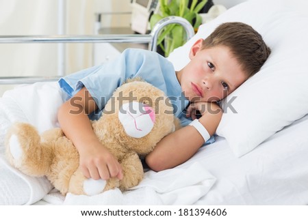 Portrait of sick little boy with teddy bear in hospital bed