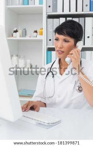 Concentrated female doctor using computer and telephone at medical office