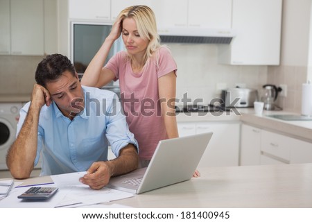 Unhappy couple with bills and laptop in the kitchen at home