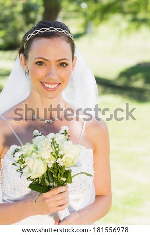 Portrait of attractive bride smiling while holding flower in garden
