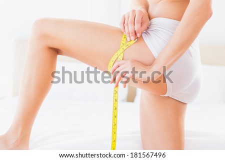Thin woman measuring her thigh at home in the bedroom