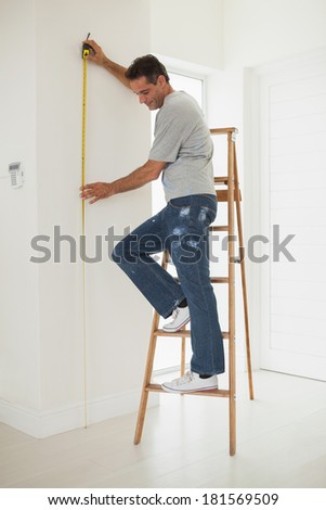 Full length side view of a man on ladder while measuring the wall at new home