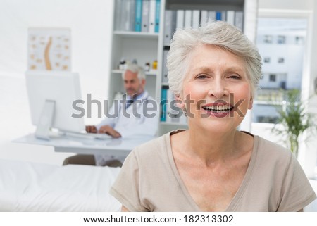 Close-up of a happy senior patient with doctor in the background at the medical office