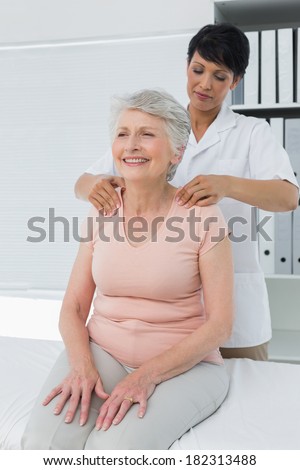 Female chiropractor massaging a senior womans shoulder in the medical office