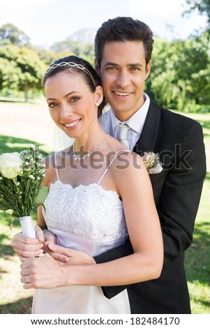 Portrait of happy groom hugging bride from behind in park