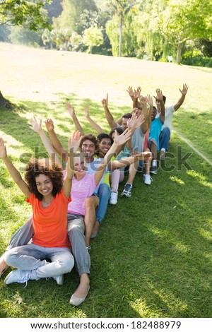 High angle view of happy friends raising hands while sitting on grass in park