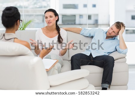 Angry couple sitting on couch talking to therapist in therapists office