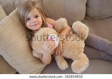 High angle portrait of a young smiling girl with stuffed toy sitting on sofa in the living room at home