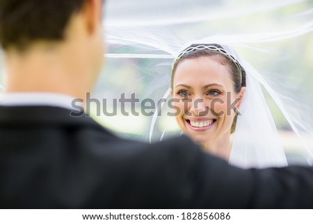 Young groom lifting bridal veil in garden