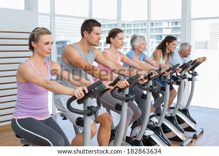 Side view of determined people working out at exercise bike class in gym